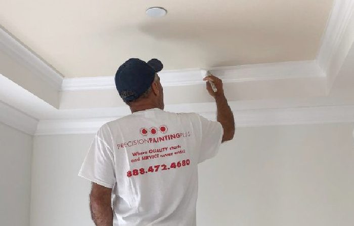 Professional painting contractor carefully applying white paint to crown molding in a residential interior, showcasing