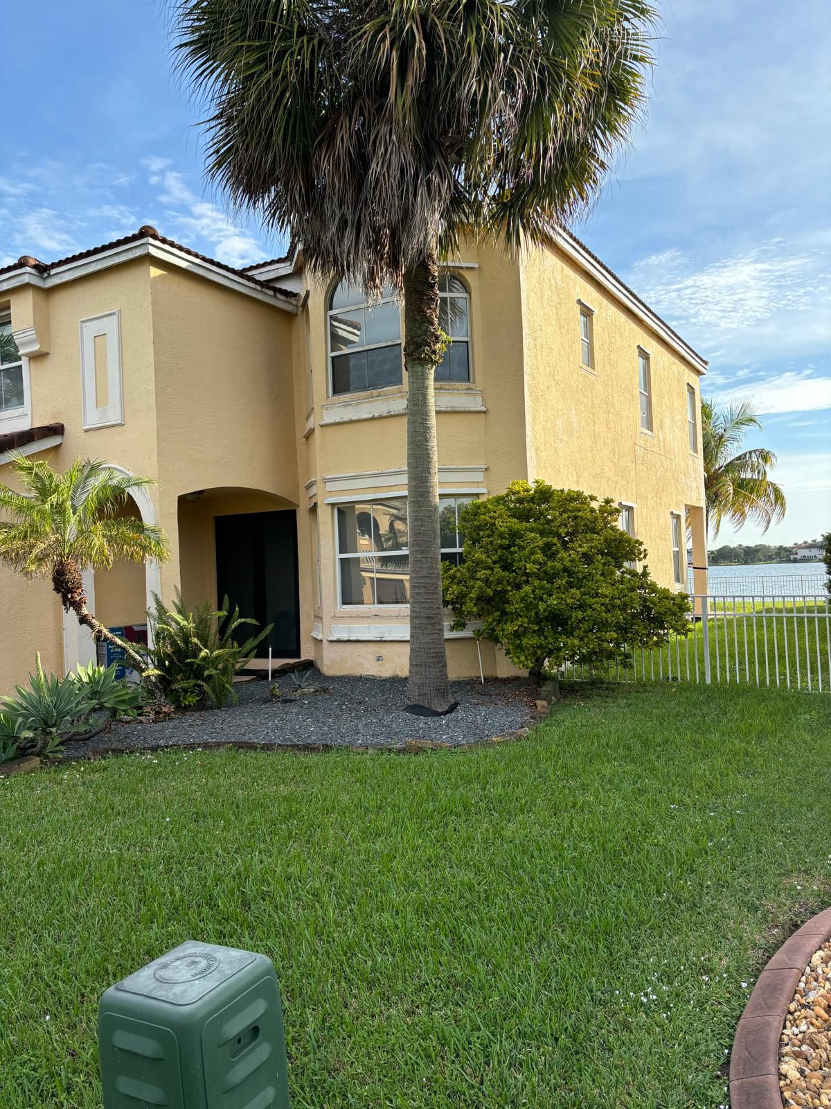 Newly painted yellow stucco home with palm trees and waterfront view, showcasing All Coast Painting's