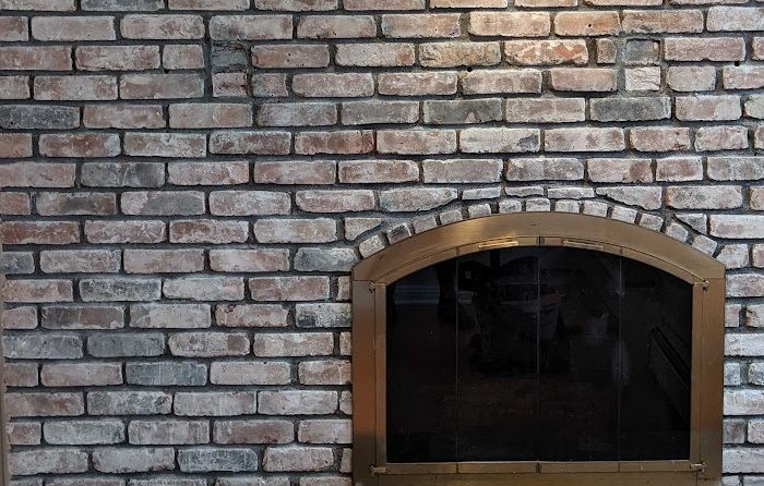 Close-up of a beautifully restored brick fireplace with a brass firebox door, showcasing All Coast
