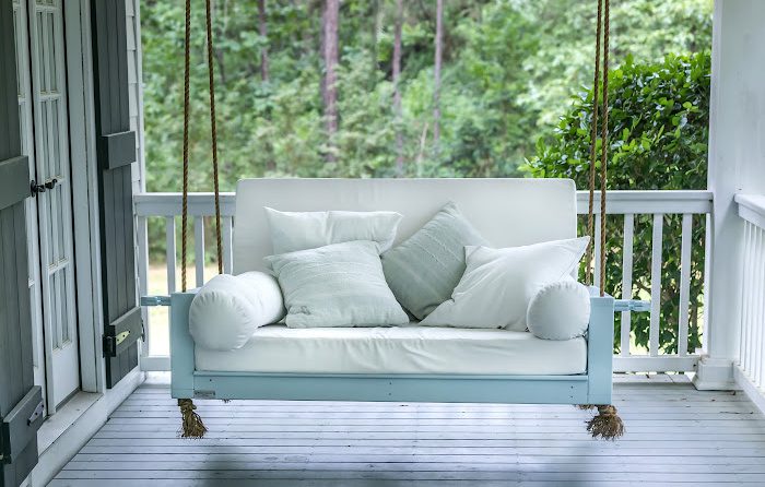Relaxing porch swing with white cushions and pillows, showcasing quality interior painting services for apartments