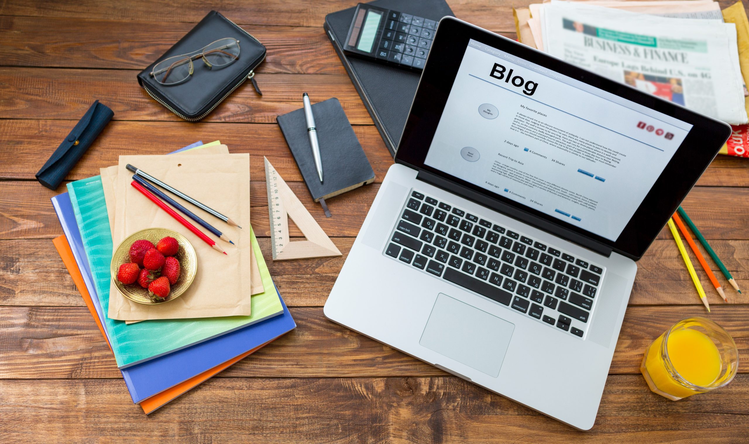 Laptop displaying a blog page surrounded by notebooks, pencils, and other office supplies, illustrating blogging